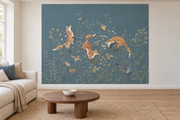 Cerfs & fleurs, motif 1 : trois renards bondissants, oiseaux, lapin et fleurs champêtres sur fond bleu ardoise, posé en papier peint dans un salon familial lumineux avec canapé en lin clair.