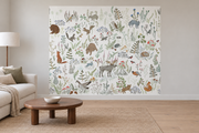 Cerfs & fleurs, motif 3 : animaux des sous-bois, élan, ours, renards, lapins, oiseaux et plantes fines sur fond blanc cassé, posé en papier peint dans un salon familial lumineux avec canapé en lin clair.