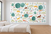 Cerfs & fleurs, motif 9 : cerfs jaunes, ours, renards, lapins et oiseaux parmi de grands arbres turquoise sur fond blanc, posé en papier peint dans une chambre d’enfant lumineuse avec lit bas et linge clair.
