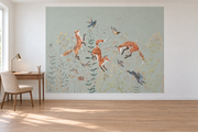 Cerfs & fleurs, motif 11 : trois renards bondissants, oiseaux, lapins gris bleuté et fleurs fines sur fond vert grisé pâle natif, posé en papier peint dans un bureau familial clair avec table de travail en bois.