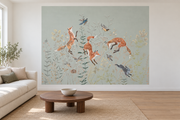 Cerfs & fleurs, motif 11 : trois renards bondissants, oiseaux, lapins gris bleuté et fleurs fines sur fond vert grisé pâle natif, posé en papier peint dans un salon familial lumineux avec canapé en lin clair.